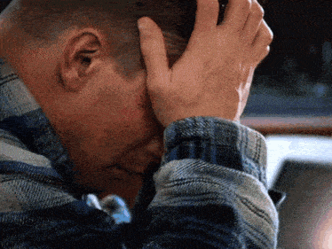 a man in a plaid shirt is covering his face with his hand