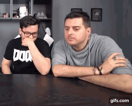 two men are sitting at a table and one of them is wearing a doom t-shirt .