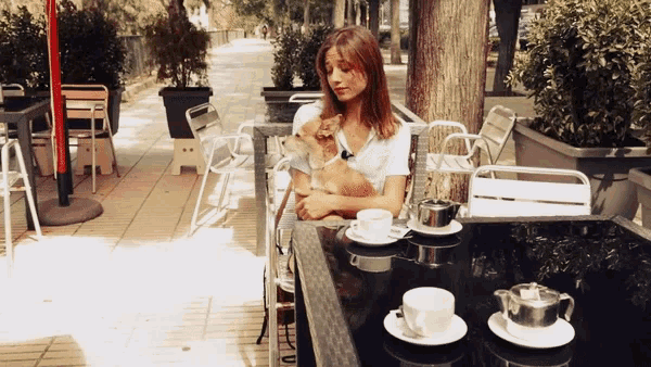 a woman sits at a table holding a cat