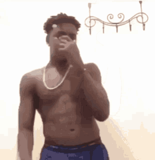a man without a shirt is covering his nose with his hand while wearing a necklace .