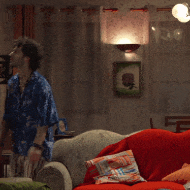 a man in a blue shirt is standing next to a red couch in a living room