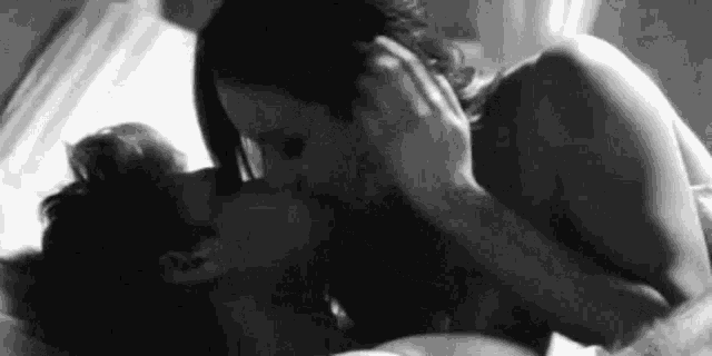 a man and a woman are kissing in bed .