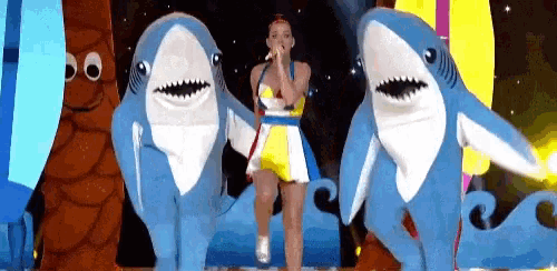 a woman is singing into a microphone surrounded by stuffed sharks on a stage