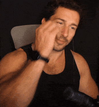 a man in a black tank top is sitting in front of a microphone with his hand on his face