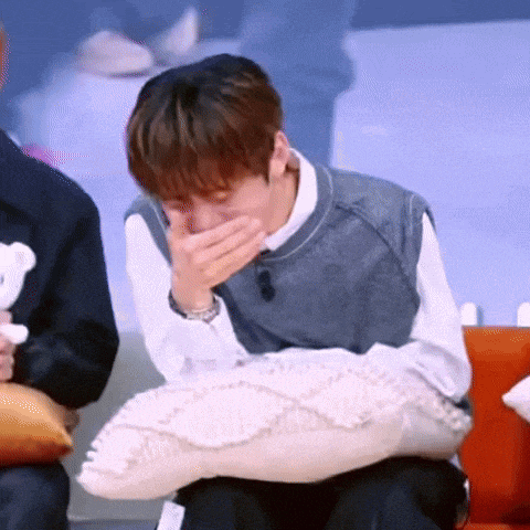 a man is sitting on a couch covering his mouth with his hand while holding a teddy bear .