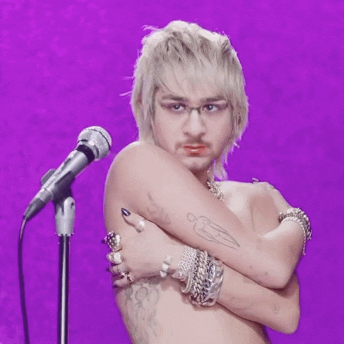 a shirtless man with a tattoo on his arm is standing in front of a microphone