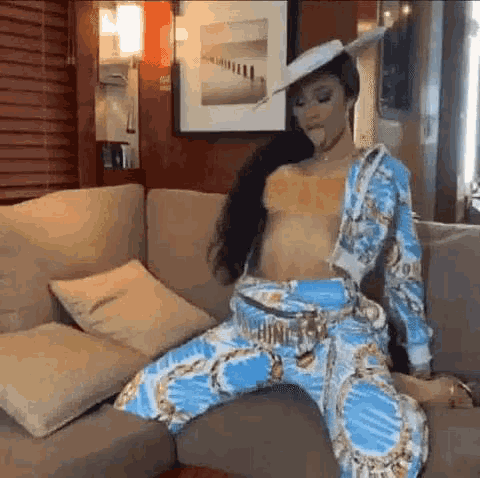 a woman is sitting on a couch wearing a hat and a crop top .