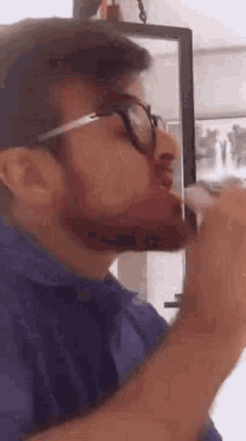 a man with a beard wearing glasses is drinking from a glass .