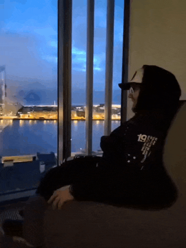 a man wearing a hoodie with the number 19 on it sits in front of a large window