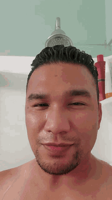 a man taking a shower with a bottle of shampoo in the background