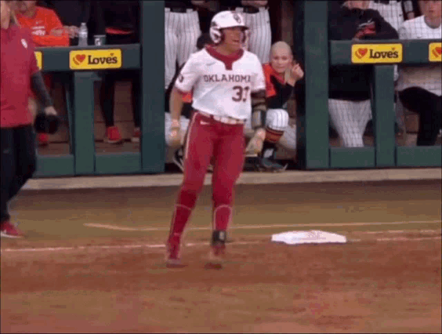 a baseball player wearing a oklahoma jersey is walking towards the base