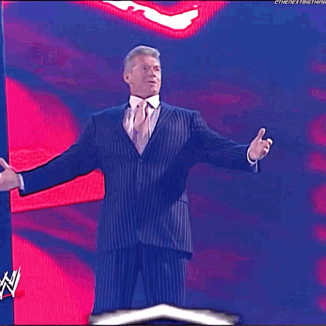 a man in a suit and tie is standing in front of a sign that says " wwe chairman mr. mcmahon "