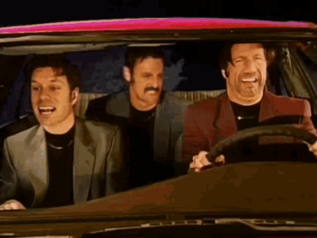 three men are sitting in a car and one of them is wearing a mustache
