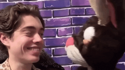 a man is smiling while holding a stuffed cat in front of a brick wall .