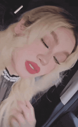 a woman with blonde hair and red lips is sitting in a car