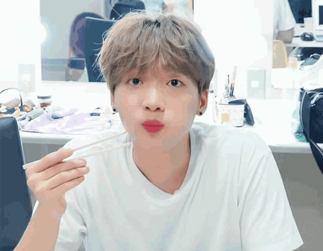 a young man eating with chopsticks with a white shirt