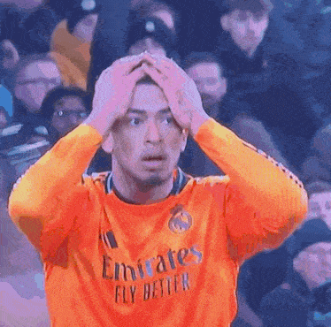a man wearing an orange emirates fly better jersey holds his head in his hands