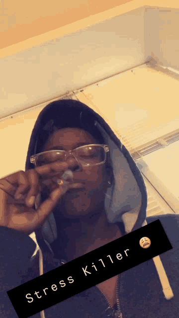 a man wearing glasses and a hoodie is smoking a cigarette and the caption stress killer