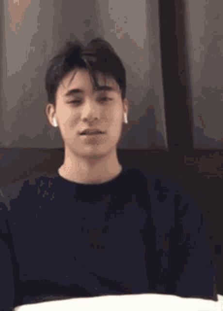 a young man wearing ear buds is sitting on a bed and making a funny face .