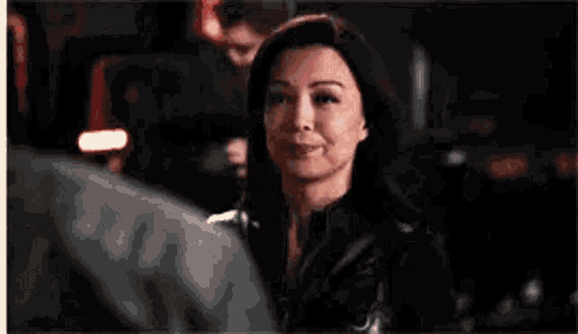 a woman in a black jacket is looking at a man in a dark room .