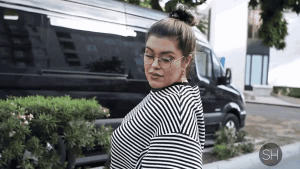 a woman wearing glasses and a striped shirt is standing in front of a van ..