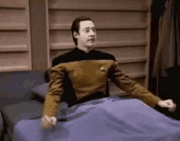 a man in a star trek uniform is sitting on a bed with his arms outstretched .
