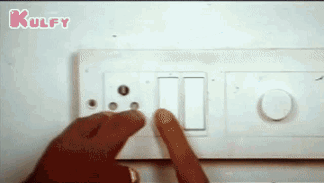 a person is pressing a button on a light switch with a kulfy logo behind them