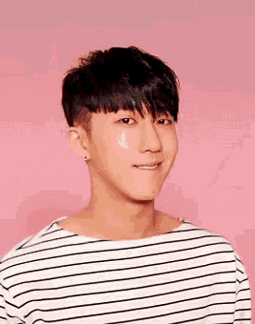 a young man wearing a striped shirt is smiling and looking at the camera on a pink background .
