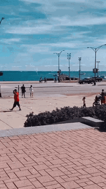 a man in a red shirt is taking a selfie on a sidewalk near the ocean