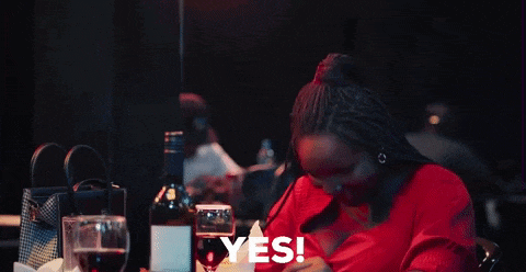 a woman in a red dress is sitting at a table with wine glasses and a bottle of wine and says yes