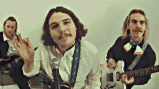 a group of men are playing guitars and singing into microphones in a room .