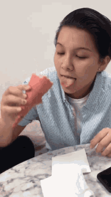 a woman in a blue shirt is eating an ice cream cone with her tongue out