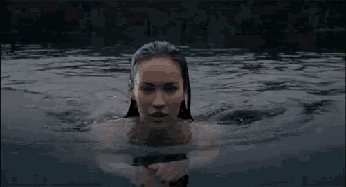 a naked woman is swimming in a lake with her head above the water .