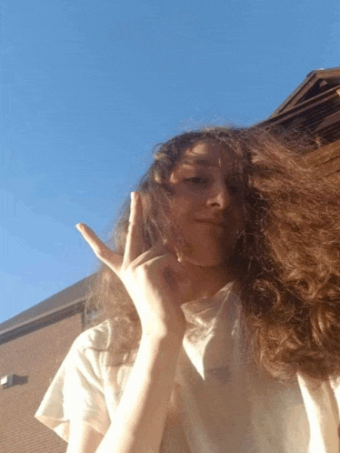 a woman with long curly hair is giving a peace sign