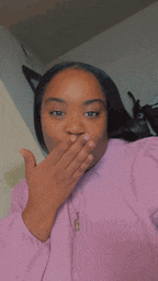 a woman in a pink shirt is blowing a kiss while covering her mouth with her hand .