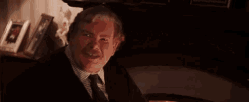 a man in a suit and tie is sitting in front of a fireplace in a dark room .