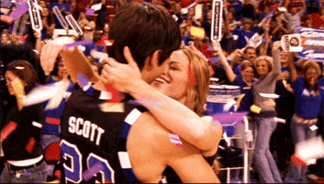 a man in a scott jersey is hugging a woman in front of a crowd