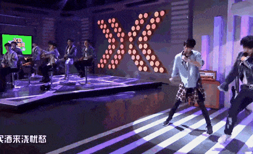 a group of young men are performing on a stage with a large x behind them