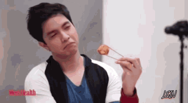 a man is holding a piece of food with chopsticks and lean is written on the bottom