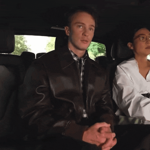 a man wearing a brown leather jacket sits next to a woman in a white shirt