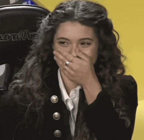 a woman with curly hair is covering her mouth with her hand and a ring on her finger .