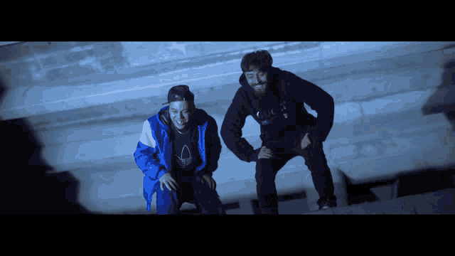 a man in a blue jacket is sitting next to another man in a black hoodie