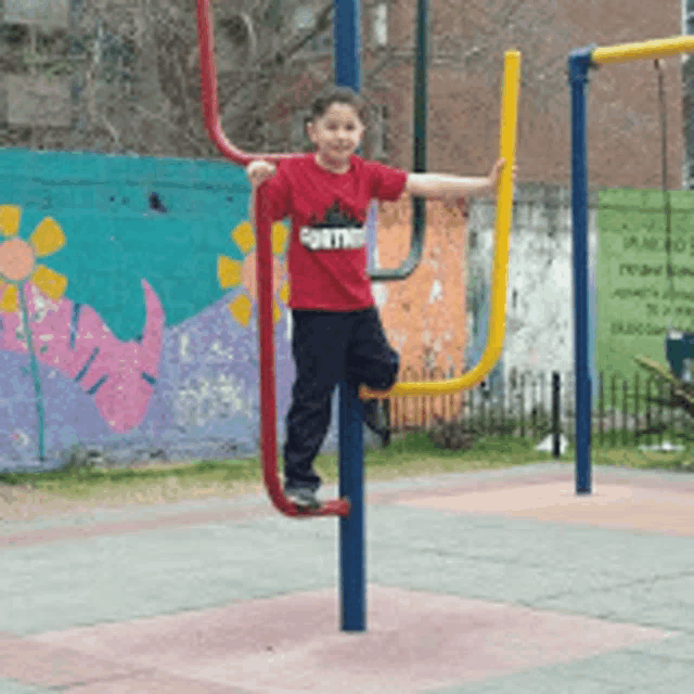 a young boy wearing a red shirt that says panther is playing in a playground