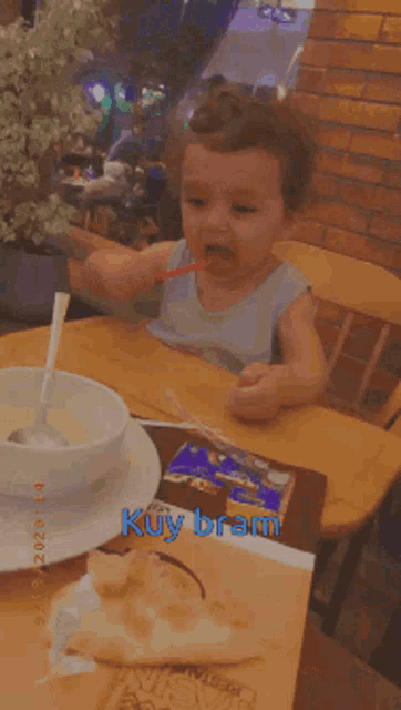 a little boy is sitting at a table with a bowl of soup and the word kuybram on the bottom