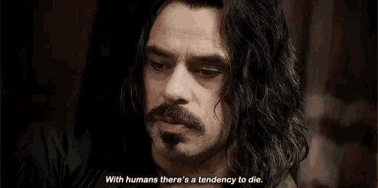 a man with long hair and a mustache is talking to another man .