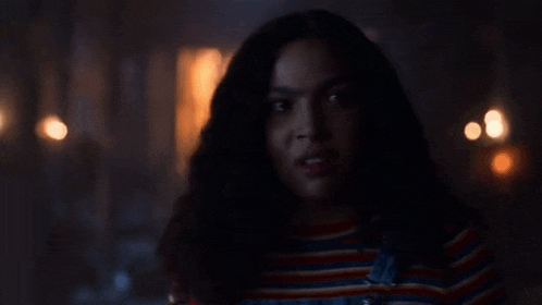 a woman in a striped shirt is standing in a dark room looking at the camera .