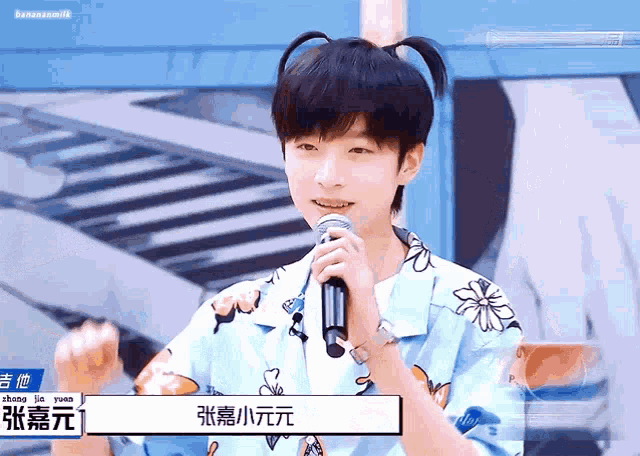 a young man with pigtails is holding a microphone in front of him