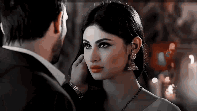 a man is touching a woman 's ear while they look at each other .
