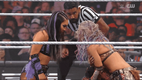 two women in a wrestling ring with a referee and a cw logo on the bottom