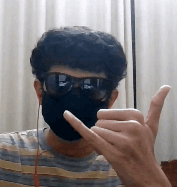 a man wearing a black mask and sunglasses is making a hand sign
